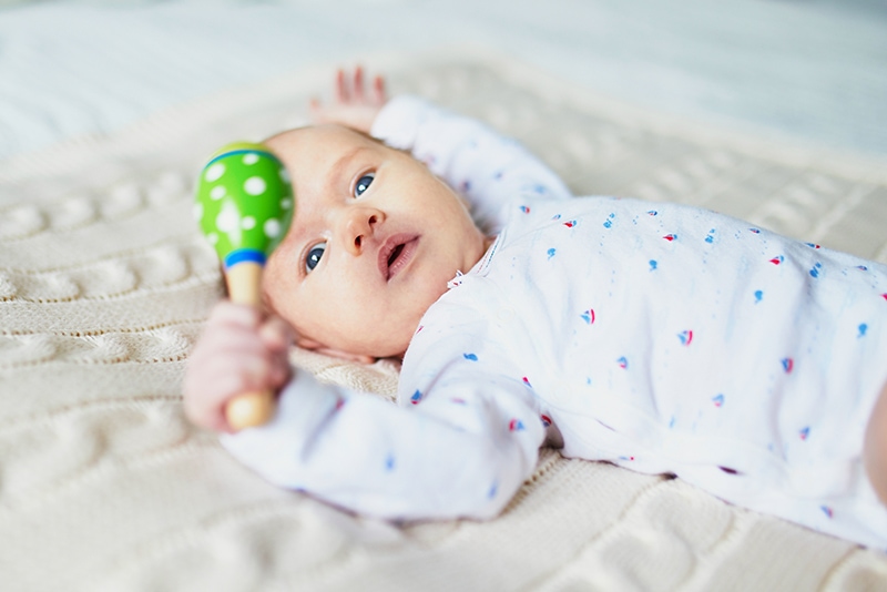 3 month old baby on back holding green rattle