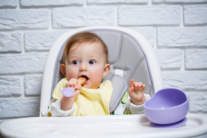 baby sitting in a high chair with the safety harness straps 10cm above the top of their shoulders.