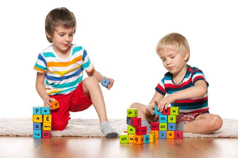 two children playing side by side with blocks, each building their own tower, which demonstrates associative play, the 5th stage in the 6 stages of play