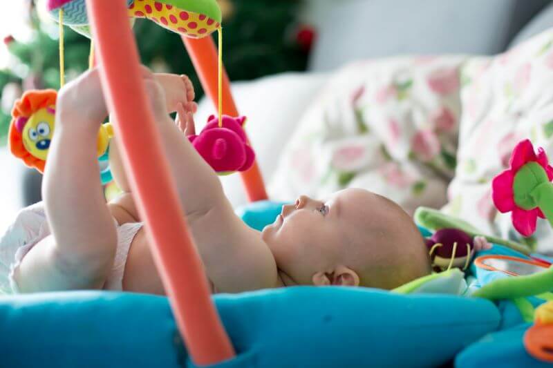 Baby lying on their back on a play gym in unoccupied play (6 stages of play, stage 1)