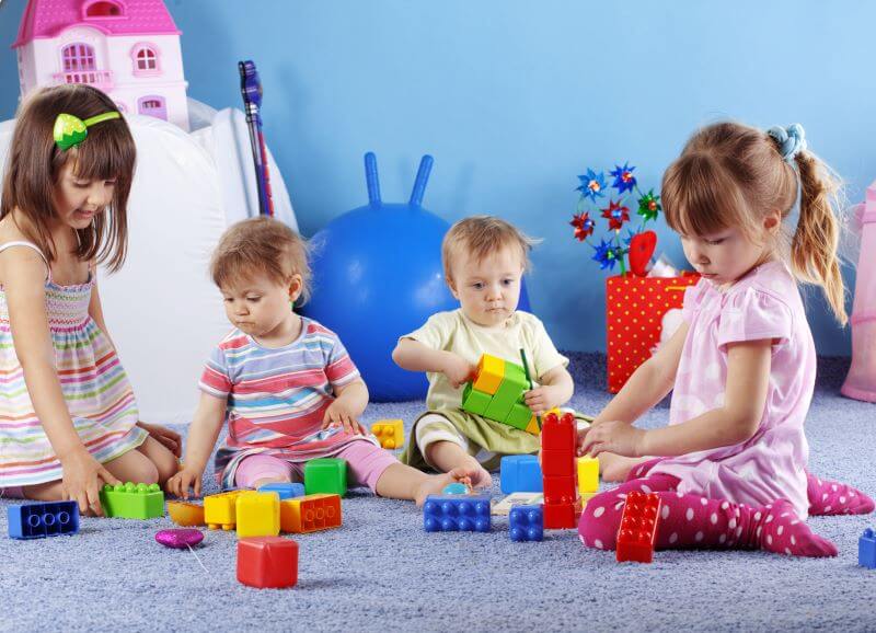 preschool children work on building their own block towers while sitting next to each other