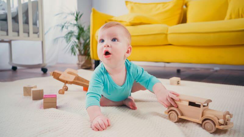 child plays on the floor with a wooden car by themselves as an example of solitary play (stage 2 in the 6 stages of play)