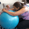 woman with a baby on a swiss ball doing tummy time to reduce the risk of flat spots on baby's head