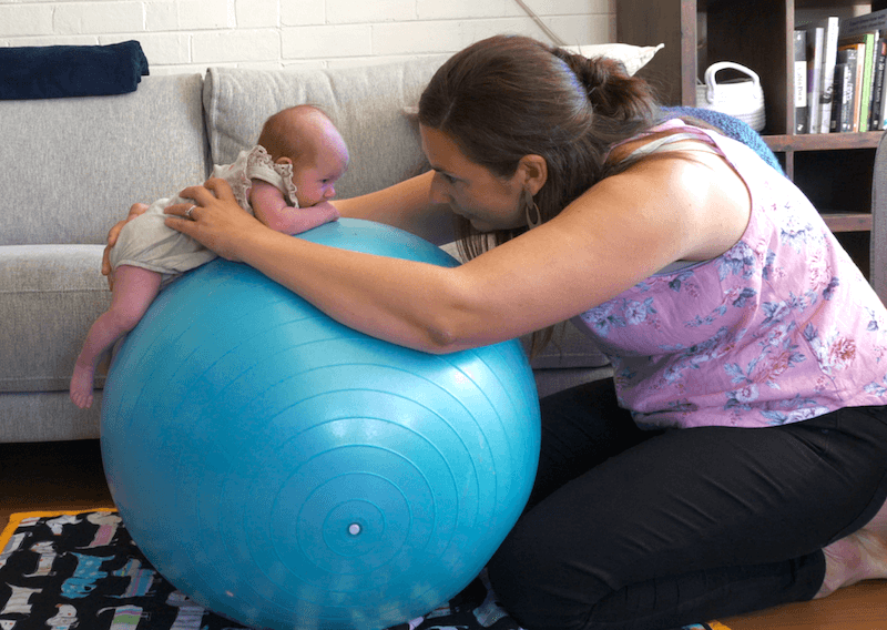 woman with a baby on a swiss ball doing tummy time to reduce the risk of flat spots on baby's head