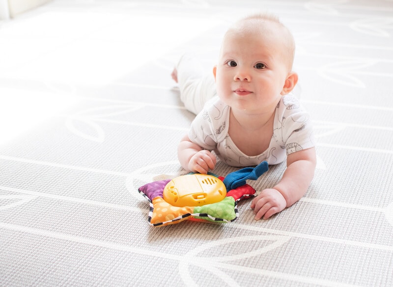 Baby lying on stomach with a musical toy on the floor in front of them