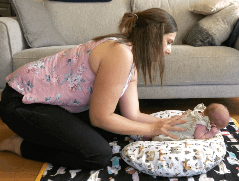 baby lies on a boppy pillow doing tummy time with woman assisting
