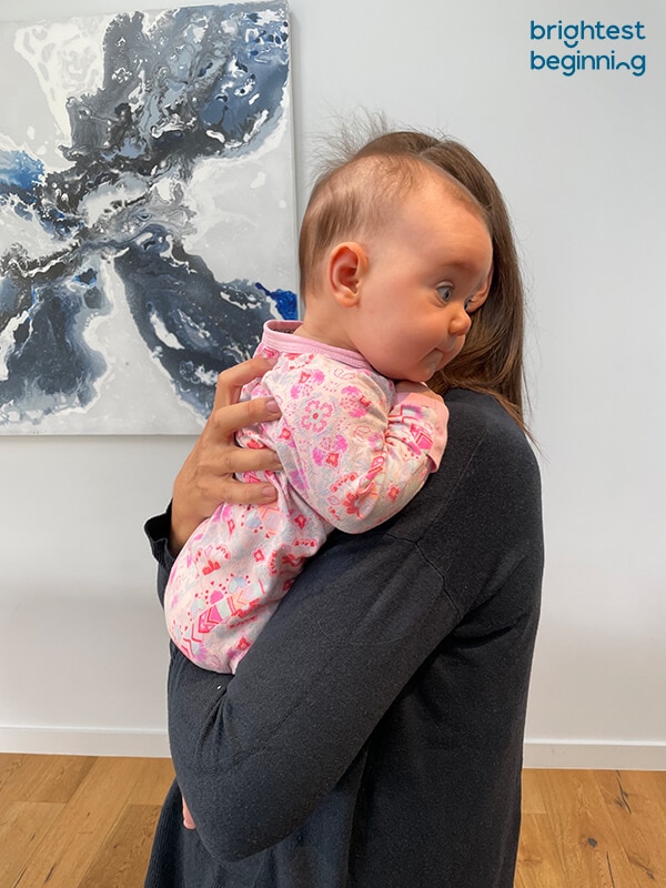Emma holding a baby over her shoulder with baby's arms raised slightly