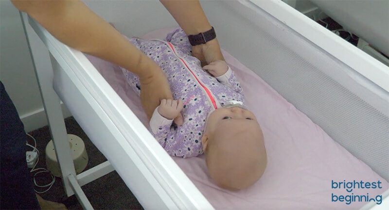 emma hubbard picking a baby up out of a crib - about to roll them onto their side