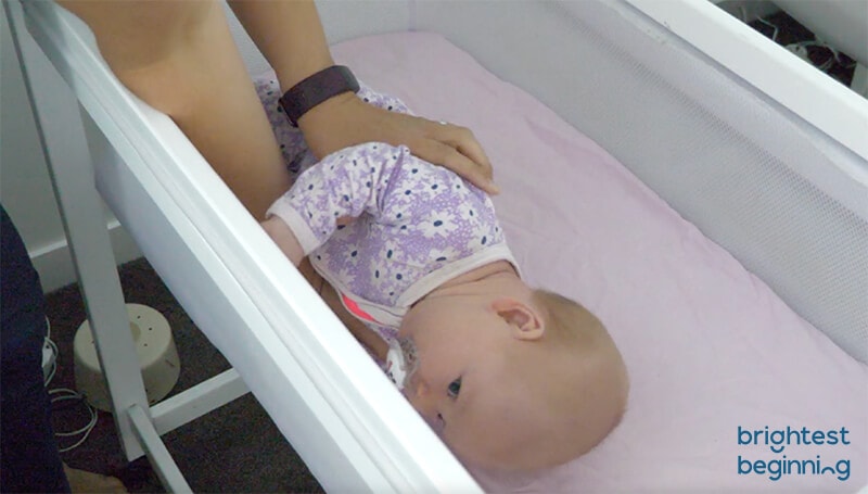 emma hubbard with a baby rolled onto their side about to lift them out of the crib