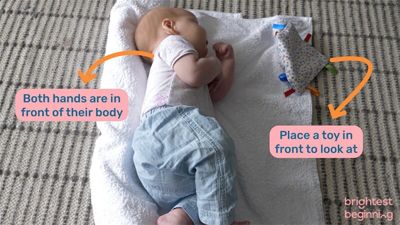 baby playing on their side with a rolled up towel behind their back and toys in front of them as an alternative to tummy time.