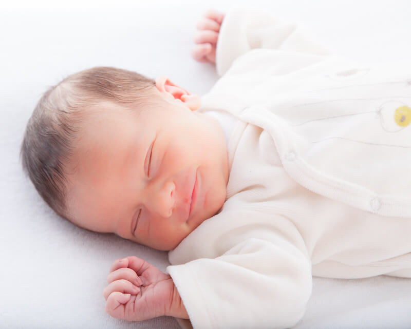 newborn baby sleeping on back with a smile on their face and arms above their head