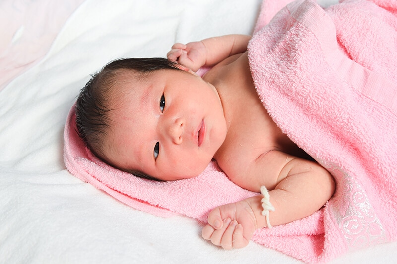 young baby lying on a towel with slight redness around their eyes, which can be a sign of tiredness.