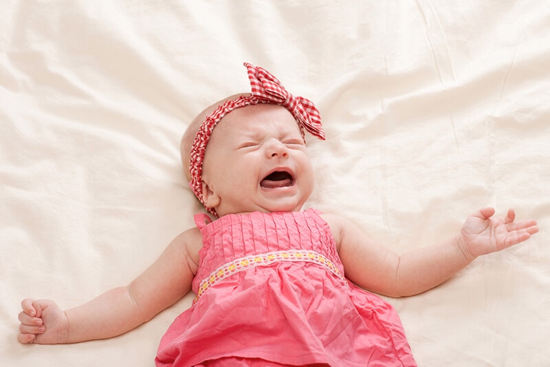 Fussy baby lying on their back crying, which may be a signal that they are tired and need their next nap.