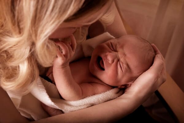 baby in mothers arms crying, possibly due to colic, but the reason isn't clear