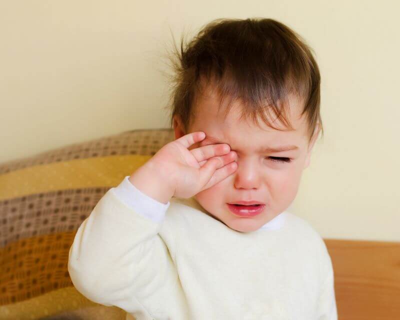 young boy waking up unhappy with a sad look on his face, rubbing eyes with one hand