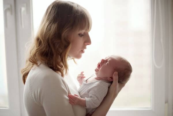 a young mother cradling her crying baby in her arms trying to settle her