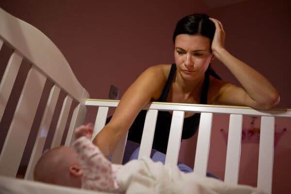 mother leaning over crib with newborn baby lying in it crying