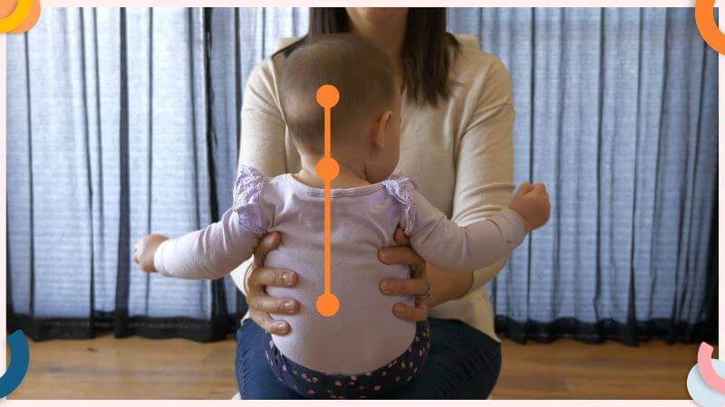 Emma Hubbard holding a baby on her lap, supporting her sides with her hands. Baby is sitting upright, with her spine, neck and head aligned.