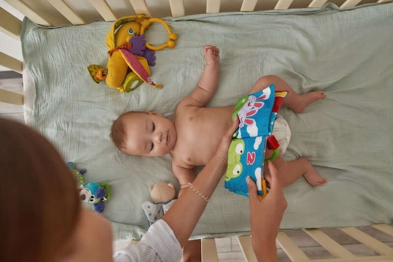 mother reading a soft book to her baby in her crib as part of their bedtime routine