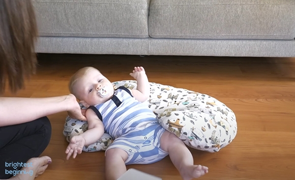 baby boy wearing a blue and white striped onesie has tipped over and is lying on his back on a boppy pillow which caught his fall.